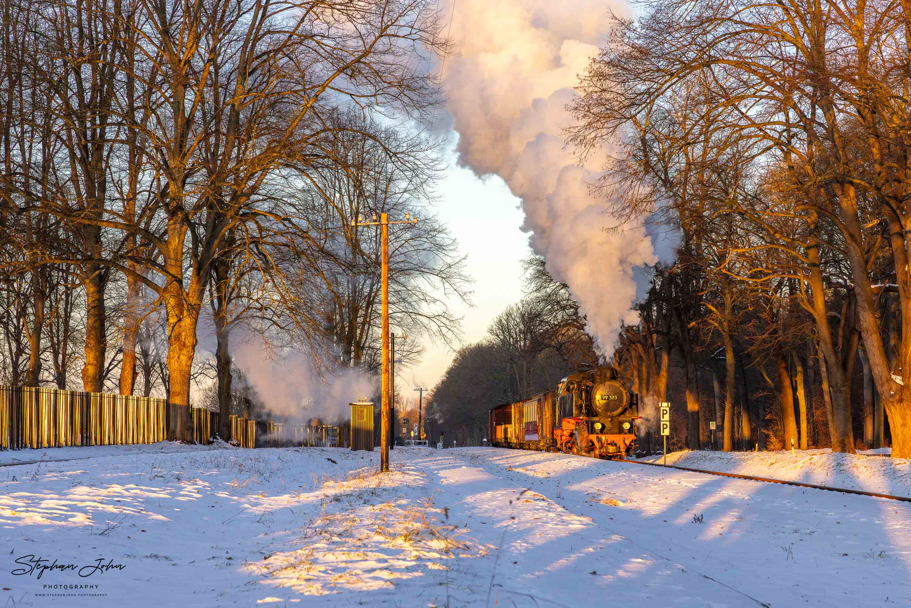 Lok 99 323 fährt im Morgenlicht mit einem GmP durch den Bahnhof Rennbahn