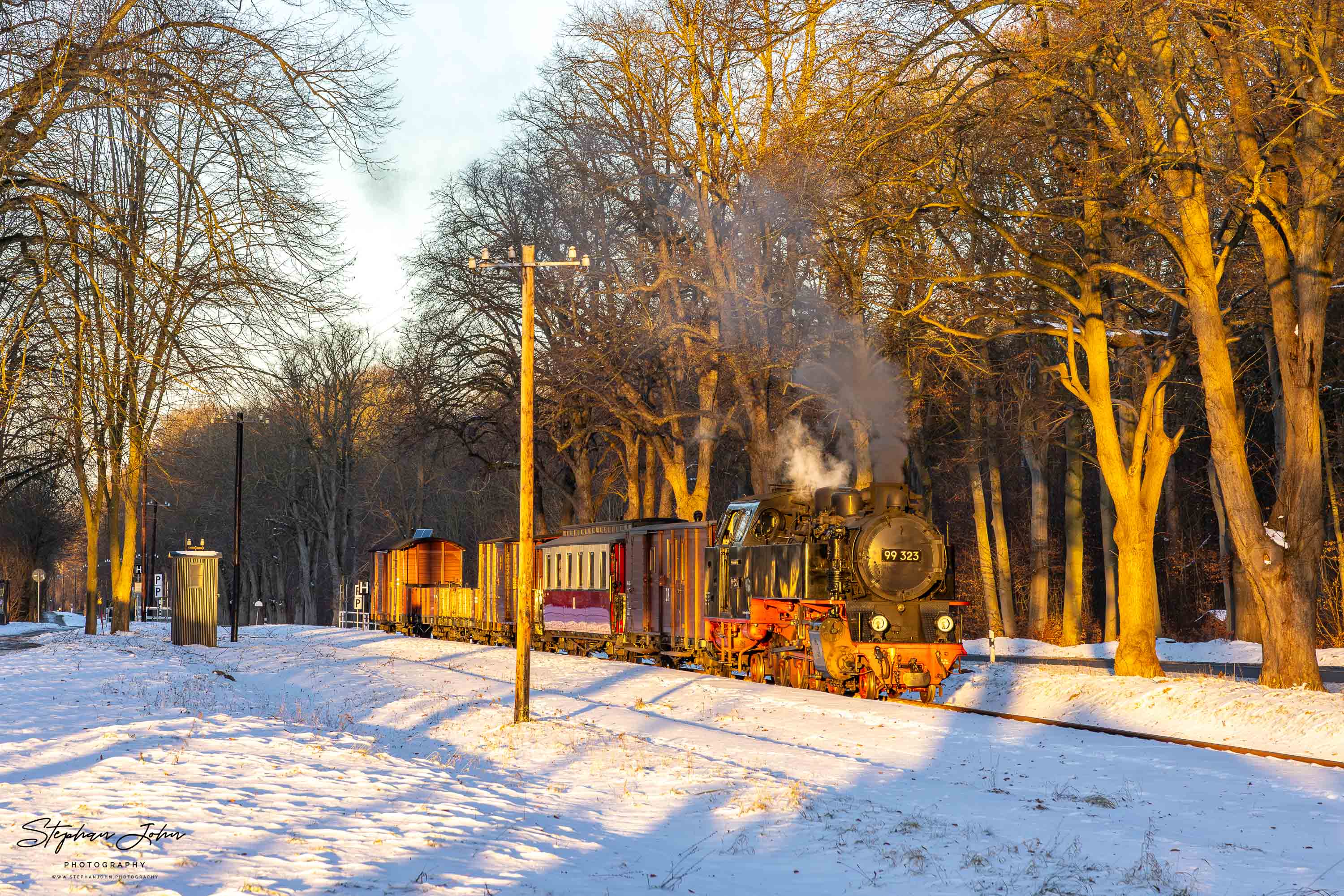 Lok 99 323 steht im Morgenlicht mit einem GmP im Bahnhof Rennbahn