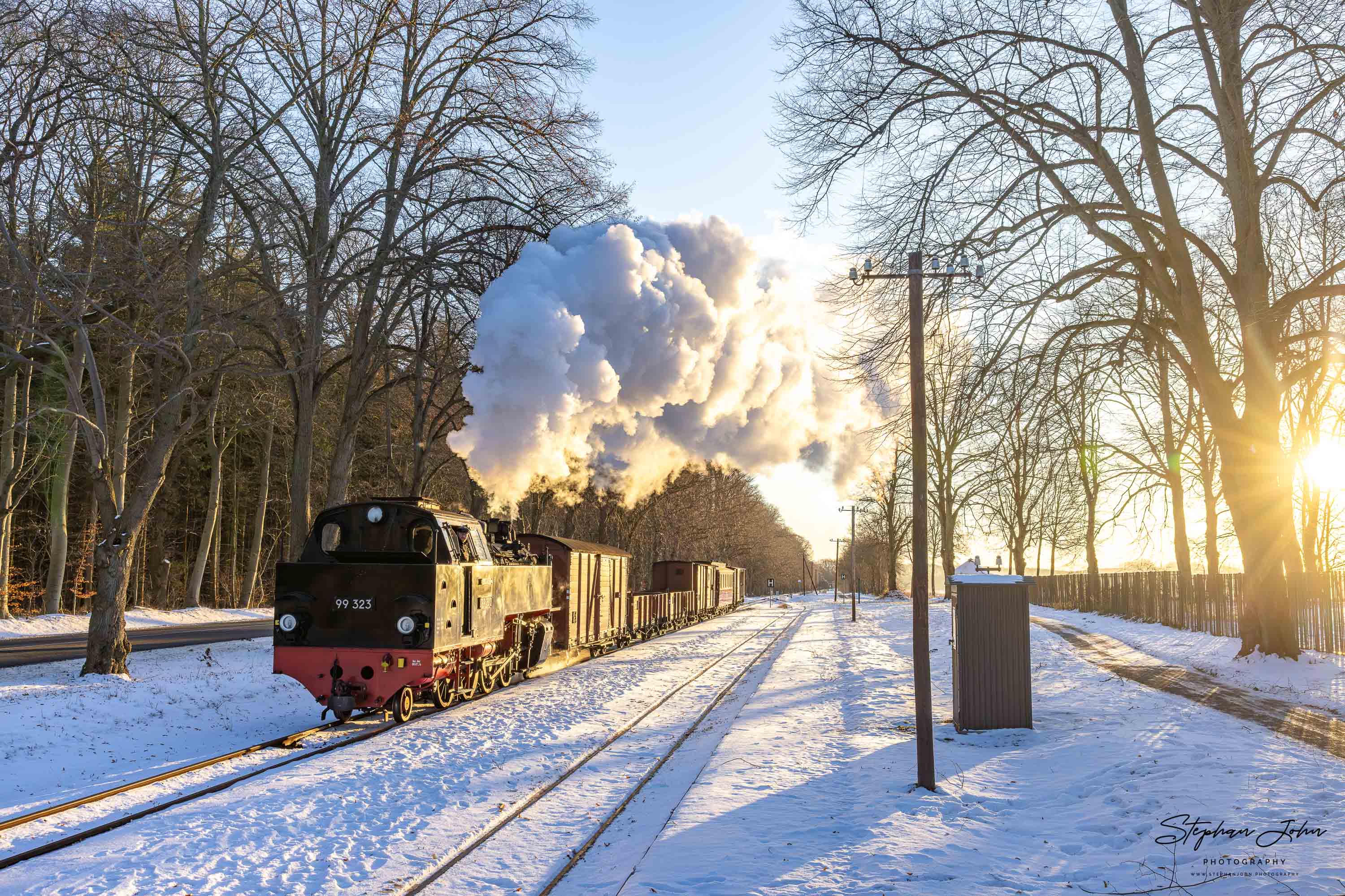 Lok 99 323 fährt im Morgenlicht mit einem GmP durch den Bahnhof Rennbahn